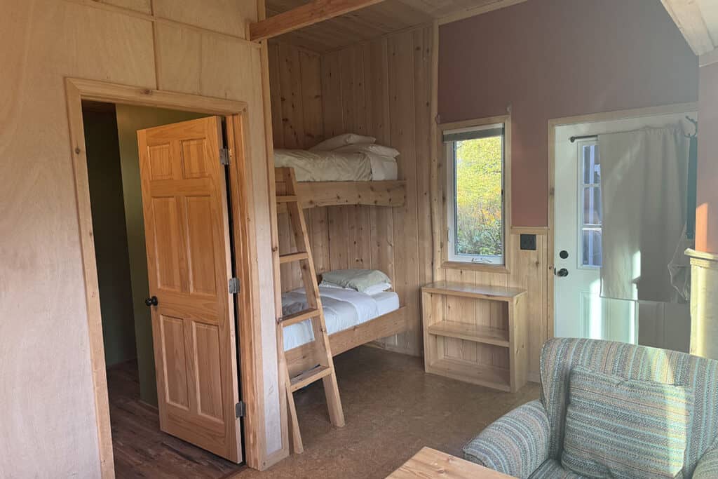 Cozy wooden cabin interior with bunk beds, window, and armchair.