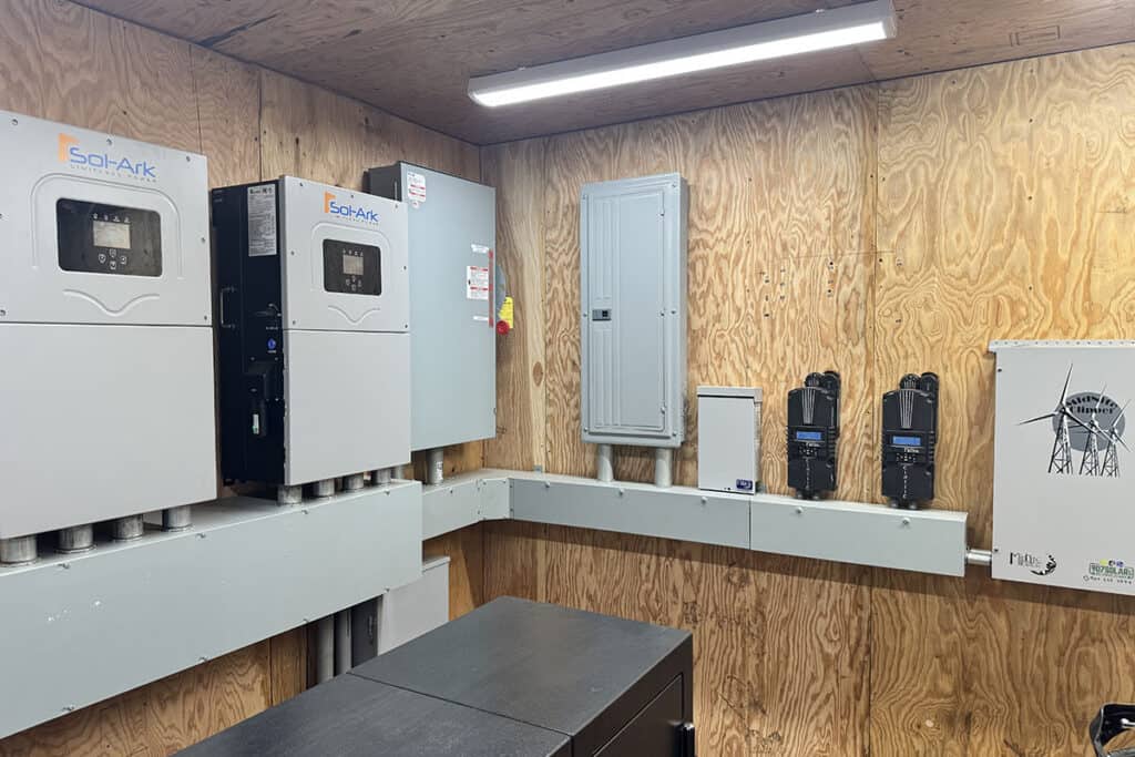 Indoor room with solar inverter and battery storage units on wooden wall.